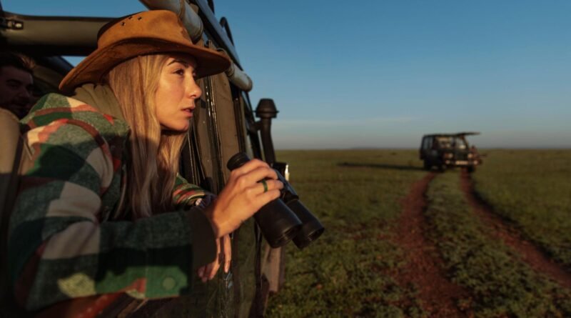 Mulher dentro de um jipe no meio da natureza com uns binóculos na mão
