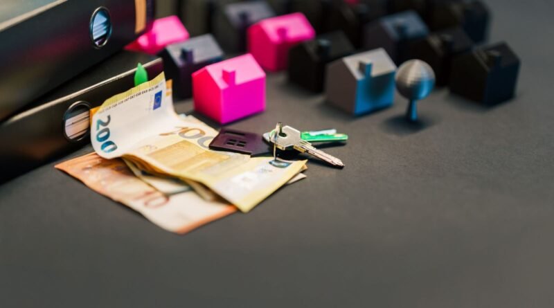 Mesa com capas, mini casas, umas chaves de casa e notas de dinheiro