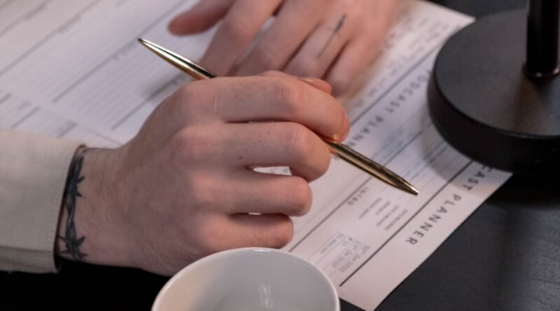 Pessoa a preencher uns papeis com caneta, com o seu café ao lado