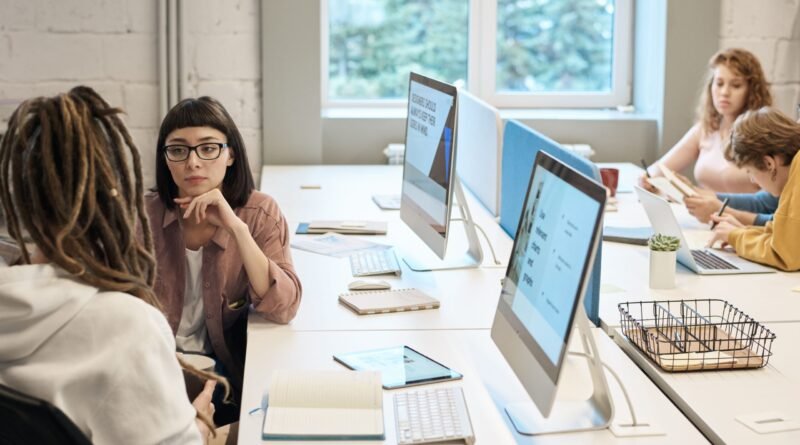 Mesa de trabalho com computadores e quatro pessoas