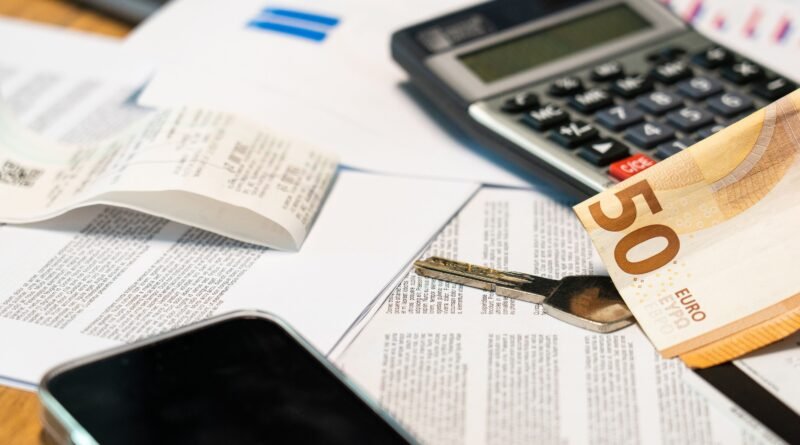 Mesa cheia de papeis, calculadora, chaves, nota de 50 euros e telemóvel