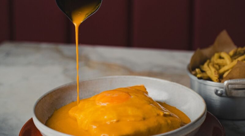 Pessoa a despejar molho na francesinha