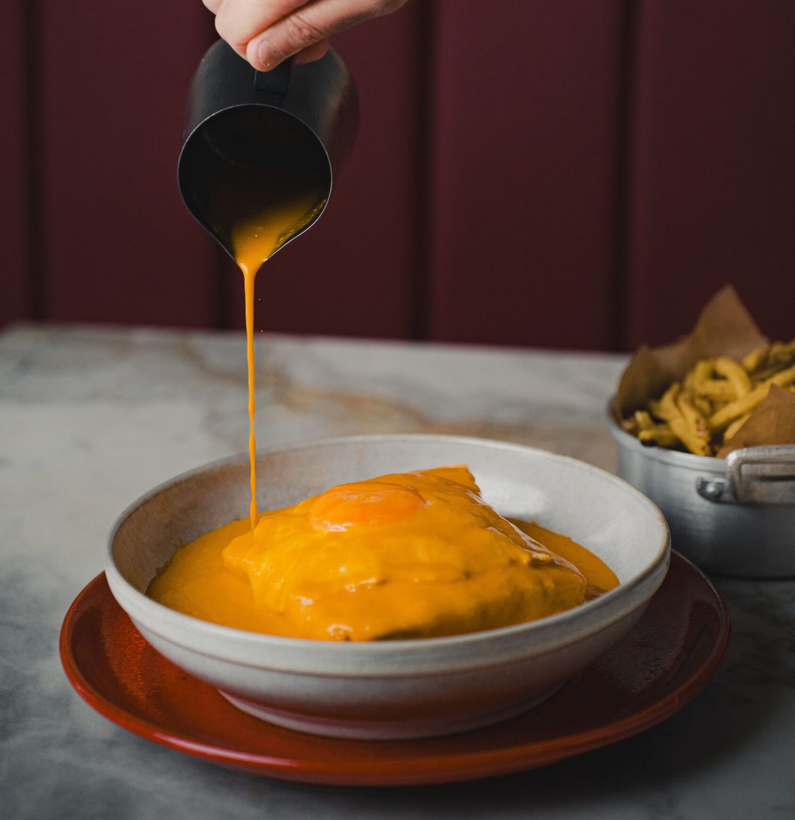 Pessoa a despejar molho na francesinha
