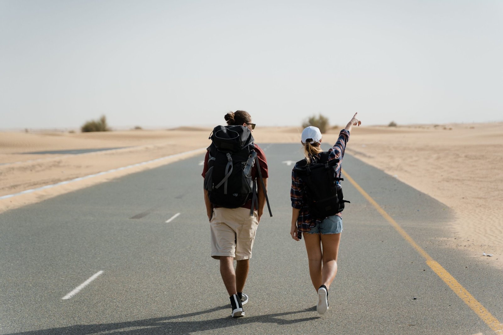 Como Viajar Quase de Graça: Estratégias Reais Que Muitas Pessoas Já Utilizam Casal a caminhar no deserto com mochilas grandes ás costas